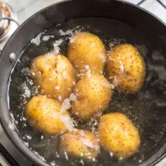 Mehrere Kartoffeln kochen in einem Topf mit sprudelndem Wasser. Sie sind fast gar, wenn sie leicht nachgeben.