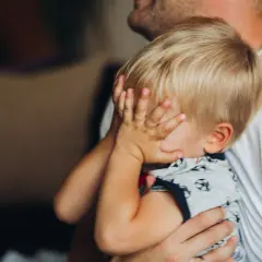 20 miesięczne dziecko budzi się w nocy, ukrywając twarz w dłoniach. Tata tuli go, próbując uspokoić.