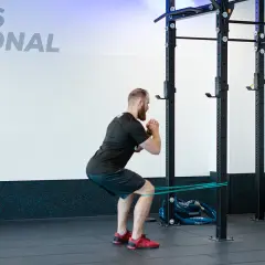 Mężczyzna wykonuje ćwiczenie spanish squat z gumą oporową wokół ud, w siłowni.