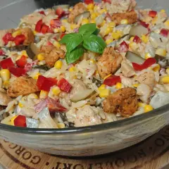 Pyszna sałatka gyros z makaronem, kurczakiem, kukurydzą, papryką i ogórkiem kiszonym, udekorowana listkiem bazylii.