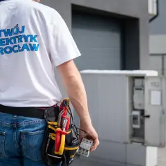 Elektryk z Wrocławia w pasie narzędziowym dokonuje odbioru instalacji elektrycznej. W ręku trzyma bezpiecznik.