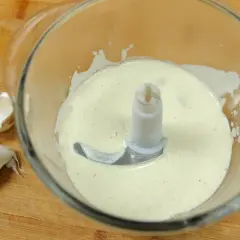 Crème d'ail onctueuse dans un mixeur, prête à être dégustée. Quelques gousses d'ail frais à côté.