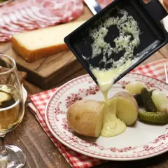 Un accord plat vin parfait : raclette fondue sur pommes de terre, cornichons, charcuterie et pain, avec un verre de vin blanc.
