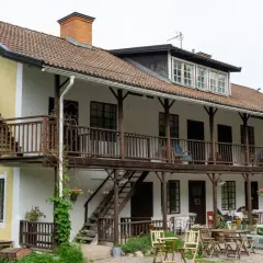 Gult hus med vita detaljer och träbalkonger. Utomhusbord och stolar står redo för gäster vid Borkhult Lapphem.