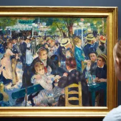 Une femme admire une peinture de Renoir représentant une scène animée de danseurs et de convives dans un jardin.