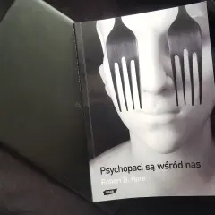Okładka książki "Psychopaci są wśród nas" z widelcami zamiast oczu na twarzy.