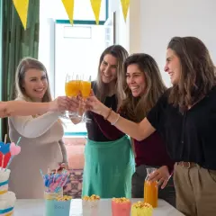 Przyjęcie baby shower: kobiety wznoszą toasty, przyszła mama w beżowym swetrze. Idealna stylizacja na baby shower to coś wygodnego i eleganckiego.