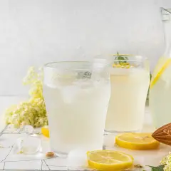 Deux verres de citronnade maison rafraîchissante avec des glaçons, des rondelles de citron, des fleurs de sureau et une carafe remplie.
