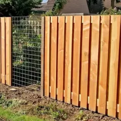 Clôture en bois reconstitué, avec des planches verticales et une section grillagée. Un chien est visible derrière le grillage.