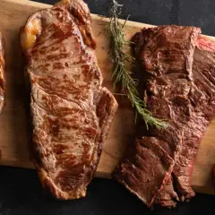 Quatre types de viande rouge grillée, dont un côte de bœuf, sont présentés sur une planche en bois.