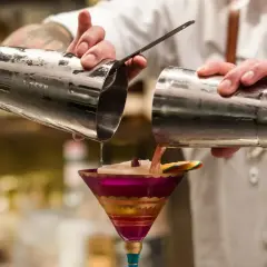 Barman przelewa drinka z shakera do drinków do ozdobnego kieliszka.