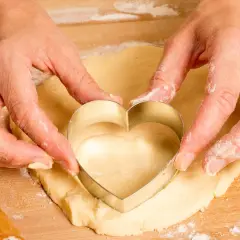 Manos cortando masa con un cortador en forma de corazón, parte del proceso de como hacer galletas caseras.