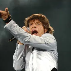 Mick Jagger, wokalista zespołu, śpiewa z mikrofonem, gestykulując ręką.