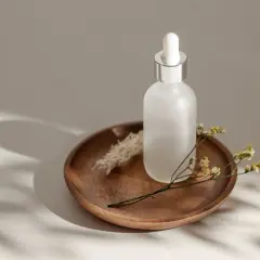 Szklana buteleczka z pipetką na drewnianej tacy, ozdobiona suchymi kwiatami. Uosobienie slow beauty, spokoju i naturalności.