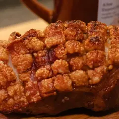 Ein knuspriger, ofenfrischer Schweinebraten mit goldbrauner Kruste liegt auf einem Holzbrett.