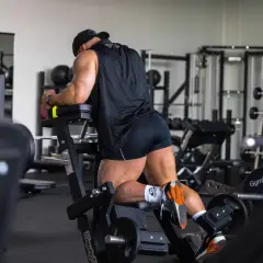 Man utför stående lårcurl på ett gym. Han har en svart tröja och shorts, och tränar sina baksida lår.