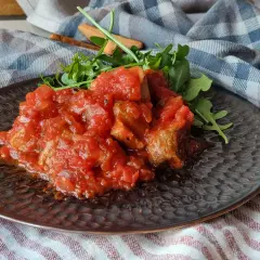 Magro con tomate, un plato casero con trozos de carne tierna bañados en una salsa de tomate casera, acompañado de rúcula fresca.