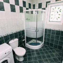 Łazienka z pralką, toaletą i narożną kabiną prysznicową. Widać syfon pod prysznic, który zapewnia prawidłowe odprowadzanie wody.
