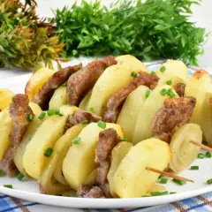 Karkówka pieczona w plastrach z cebulą i ziemniakami na patyczkach, posypana szczypiorkiem.