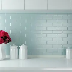 Un mazzo di rose rosse in un vaso bianco su un piano di lavoro, con barattoli bianchi e uno sfondo di piastrelle azzurre. Ottime opinioni per dipingere piastrelle cucina.