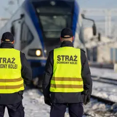 Dwóch funkcjonariuszy Straży Ochrony Kolei w kamizelkach odblaskowych stoi przed pociągiem. Działają na mocy ustawy o straży ochrony kolei, zapewniając bezpieczeństwo.