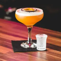 Orzeźwiający drink z marakują i prosecco, ozdobiony plasterkiem owocu, obok kieliszek z bąbelkami. Idealny na letnie wieczory.