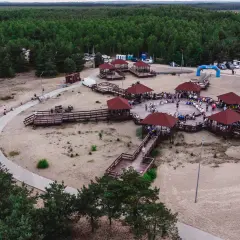 Drewniane zadaszone altany i ścieżki na piaszczystym terenie w miejscowości Klucze, otoczone lasem.