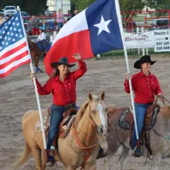 Kobiety na koniach niosą flagi USA i Teksasu. Teksas, z jego bogatą historią i dużą liczbą ludności, świętuje na rodeo.