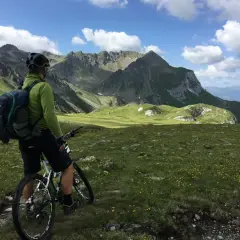 Rowerzysta w zielonej bluzie i kasku z plecakiem na plecach podziwia alpejski krajobraz. Idealny plecak na rower na taką wyprawę.