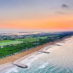 Alba sul mare veneto, con la spiaggia dorata, pineta rigogliosa e lagune all'orizzonte.