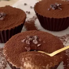 Delicioso postre con ricota, cubierto de cacao y trocitos de chocolate. Una cuchara dorada se hunde en uno de ellos.