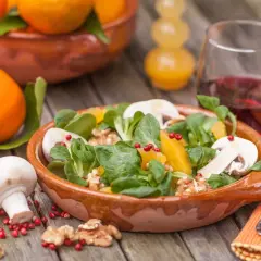 Ein frischer Wintersalat mit Orangen, Pilzen und Walnüssen in einer Terrakotta-Schale. Daneben liegen frische Orangen und ein Glas Rotwein.