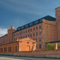 Dawny księży młyn w Łodzi, ceglany kompleks przemysłowy z wieżą, pod błękitnym niebem.