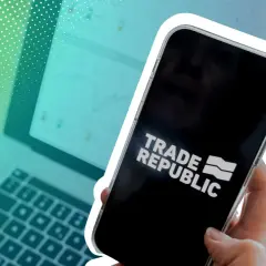 Hand hält Smartphone mit Trade Republic Logo. Im Hintergrund Laptop mit Charts. Die Trade Republic Einlagensicherung gibt Sicherheit.