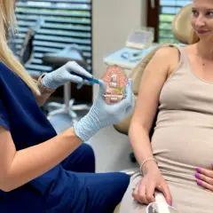 Dentystka pokazuje ciężarnej pacjentce prawidłową higienizację zębów w ciąży na modelu szczęki.