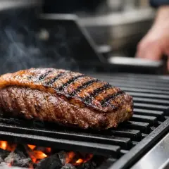 Un beau steak est en cuisson barbecue gaz, avec des marques de grill parfaites et de la fumée qui s'en dégage.