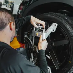 Mecánico ajusta un sensor en la rueda de un coche. Averigua cuanto cuesta alinear un coche para un manejo seguro.
