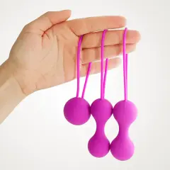 Main d'une femme tenant trois boules de geisha violettes avec des cordons.