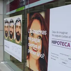 Anuncios de hipotecas en un escaparate. Uno muestra tres hombres y pregunta "¿Te imaginas no pagar cuotas el primer año?". Otro, con una mujer, dice "Deja de imaginar. No pagues cuotas el primer año. HIPOTECA 12X0". Se ve un **euribor forecast** en la ...