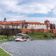 Zamek Królewski na Wawelu nad Wisłą, z łodzią i spacerującymi ludźmi.