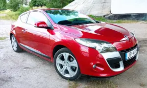 Czerwone Renault Megane Coupe 3 na tle betonowej konstrukcji i zieleni.