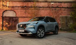 Szary Nissan X-Trail stoi przed starą ceglaną ścianą z zardzewiałymi drzwiami.