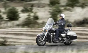 Mężczyzna w kasku jedzie na lśniącym motorze chopper, przemierzając pustą drogę wśród drzew.