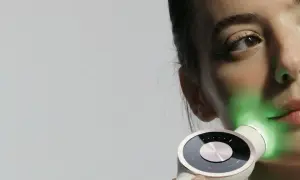 Une femme utilise un appareil de luminothérapie LED pour le visage, projetant une lumière verte apaisante.