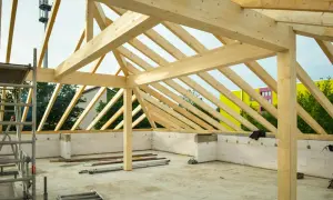 Struttura in legno per la realizzazione di tetti, con travi a vista e muri in blocchi di cemento. In sottofondo, attrezzature da cantiere.