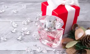 Eleganckie perfumy w szklanej butelce, czerwone pudełko z kokardą i ozdoby. Idealny pomysł, jak zapakować perfumy na prezent.