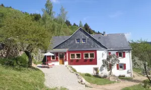 Maison de campagne avec terrasse et parasol, idéale pour un camping à la ferme dans les Vosges. Le soleil brille sur ce paysage verdoyant.