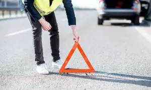 Hombre con chaleco reflectante coloca un triángulo de señalización tras una detención de coche en la carretera.