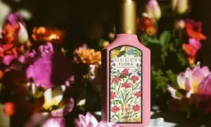 Różowa butelka Gucci Flora Gorgeous Gardenia otoczona bujnymi, kolorowymi kwiatami.
