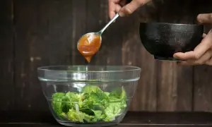 Ein Löffel mit braunem Salatdressing tropft in eine Schüssel mit knackigem Salat.